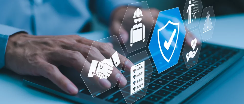 Close up of a person typing on a laptop with floating safety and compliance icons overlaid on the screen. A highlighted shield with a check mark appears alongside symbols for worker protection, checklist, handshake, and risk warning.