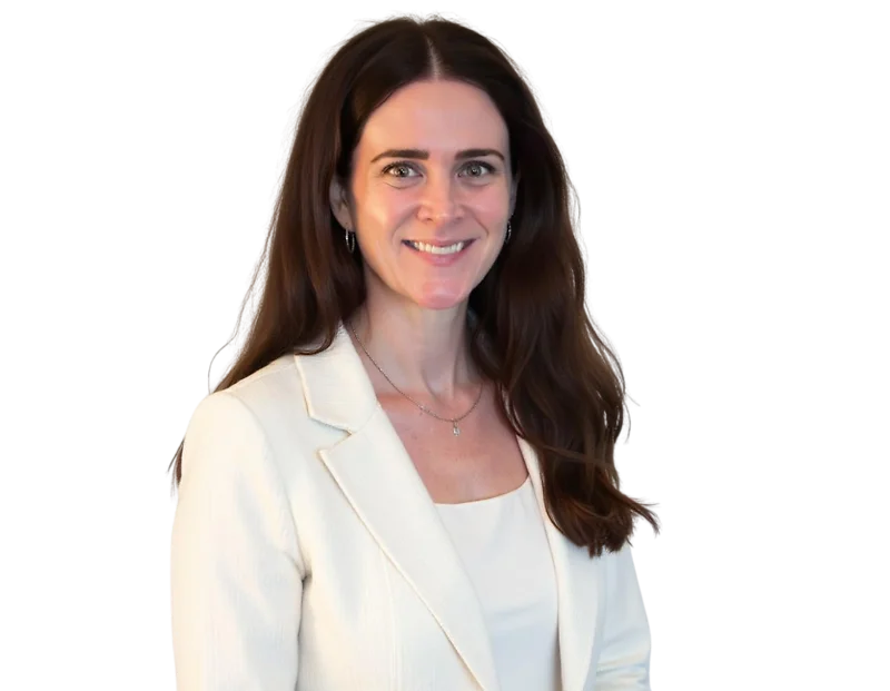 Smiling professional woman with long dark brown hair wearing a cream blazer over a light top, accessorized with small hoop earrings and a delicate necklace. She stands against a transparent background with a warm, confident expression suitable for a corpo