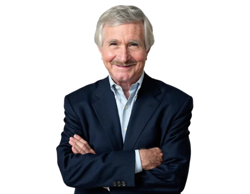 John Doyle wears a dark suit and light blue shirt, smiling with arms crossed against a light blue and white geometric background.