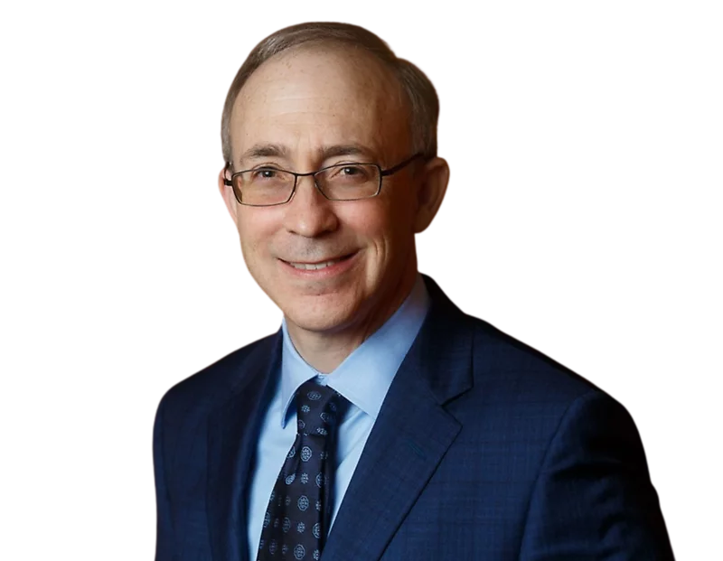 Eric Proser wearing glasses, a blue suit, light blue shirt, and patterned dark tie against a plain background.