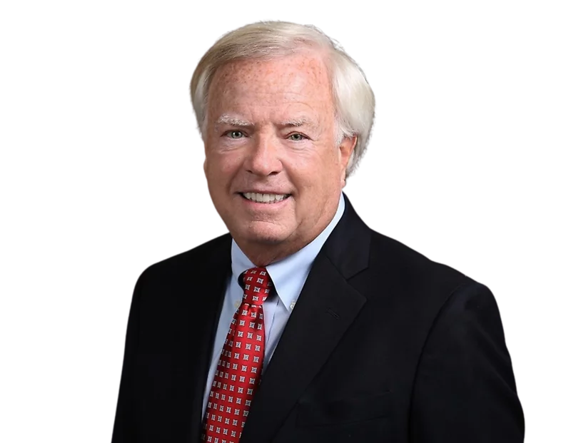 Pat Tyson wearing a dark suit, light blue shirt, and red patterned tie against a plain background.