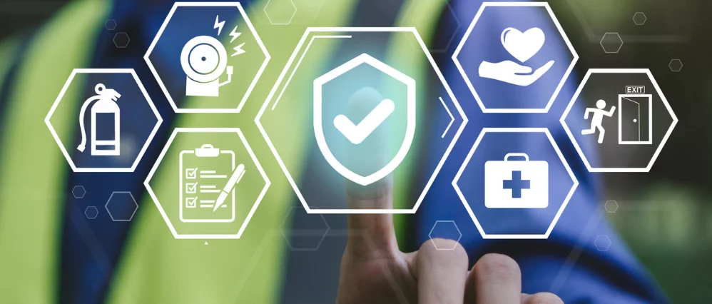Close up of a worker in a high visibility vest touching a virtual shield icon with a check mark at the center of floating safety symbols. Surrounding hexagon icons show a fire extinguisher, alarm, checklist, heart in hand, medical kit, and emergency exit