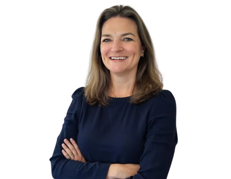 Professional head-and-torso portrait of Missy Spainhour, smiling with her arms crossed. She is wearing a dark long-sleeved top and standing against a light, modern background with soft blue geometric accents.