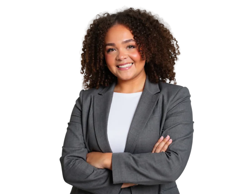 A professional portrait of a woman with shoulder-length curly dark hair smiling directly at the camera. She is wearing a gray business suit jacket over a light-colored blouse and stands with her arms crossed in a confident, approachable pose.