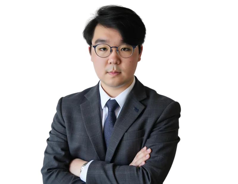 Professional man with short black hair and round glasses wearing a gray suit, white dress shirt, and dark blue tie, standing with arms crossed against a transparent background. He has a serious, focused expression that conveys professionalism and confiden
