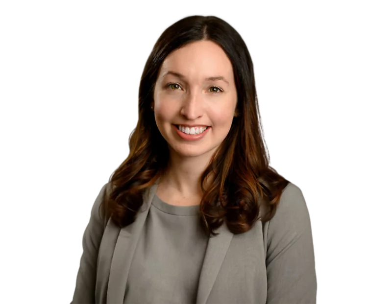 A professional headshot of Brett Swanson with long, wavy brown hair wearing a gray blazer and a matching blouse, smiling at the camera. The background has been removed, isolating her against a transparent backdrop, making it ideal for business or corporat