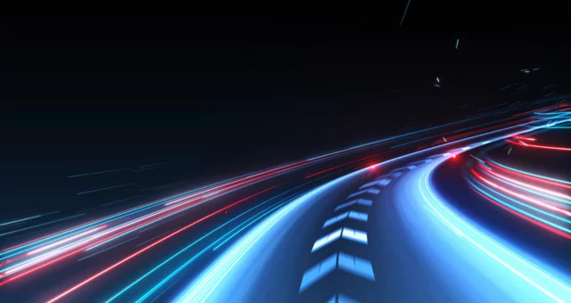 Futuristic illustration of a curving road with glowing blue and red light trails, suggesting high-speed motion through a dark environment. The dynamic perspective conveys themes of technology, innovation, and rapid progress.
