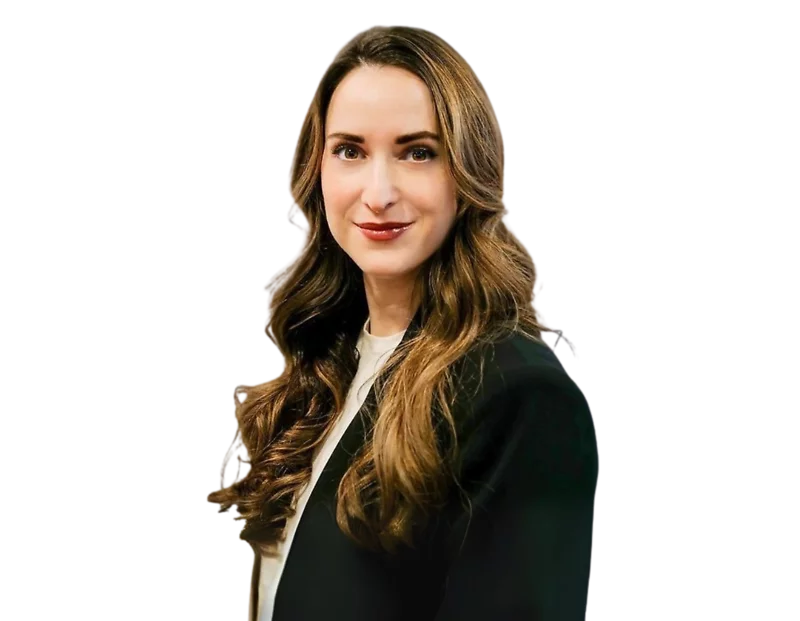 Confident woman with long wavy brown hair wearing a black blazer over a white top, posing against a transparent background. She has a poised expression and a professional appearance suitable for corporate or business profiles.