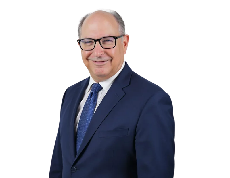 Remy Kessler smiling in a formal headshot. He is wearing a dark blue suit, white shirt, and textured blue tie, posed against a plain background.