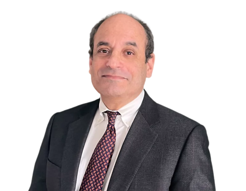 Older man with a receding hairline wearing a dark checkered suit, white dress shirt, and a red paisley tie, posing with a slight smile against a transparent background. His formal appearance and composed posture reflect a professional or executive role.