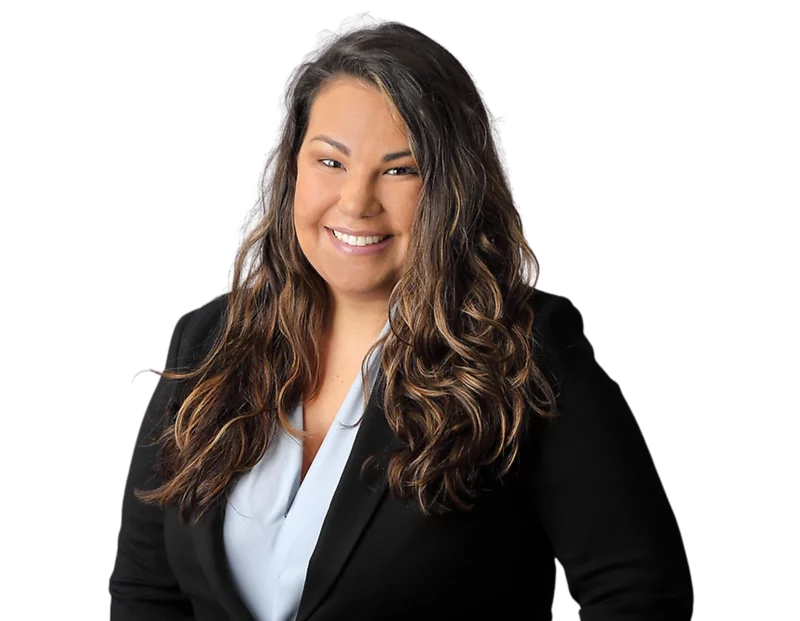 Professional headshot of Amanda Morejon smiling, wearing a light blue blouse under a black blazer, with long wavy hair, posed against a softly blurred light background.
