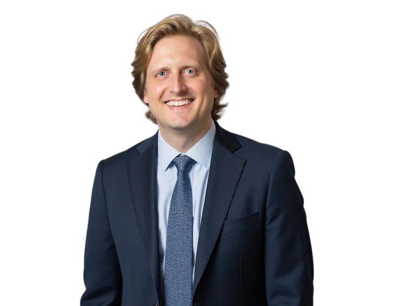 Evan Jarrold smiling in a dark navy suit with a light blue shirt and patterned tie, posed against a transparent background in a professional headshot style.