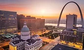 Sunrise over downtown St. Louis, Missouri, with the Gateway Arch towering above the Mississippi River. The historic Old Courthouse stands in the foreground, framed by modern office buildings.