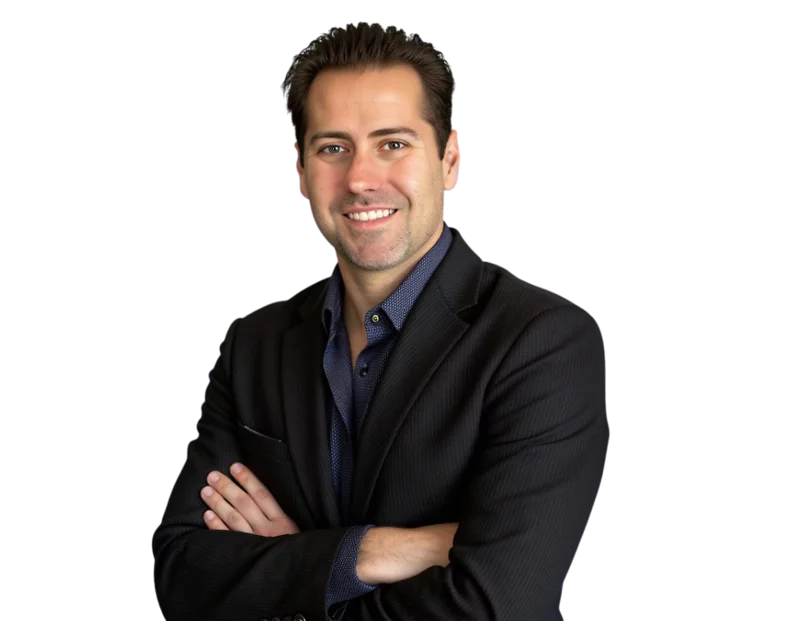 Smiling man with dark, neatly styled hair wearing a navy button-up shirt and black blazer, standing with arms crossed against a transparent background. He appears confident and approachable, dressed in business attire.