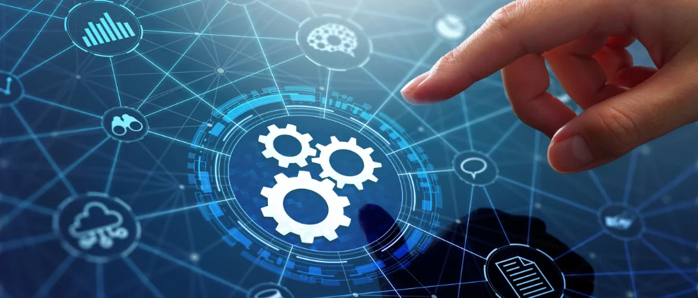 Close up of a hand interacting with a digital interface featuring interconnected network lines and icons. At the center, a glowing circular display highlights three gear symbols, representing systems and processes.