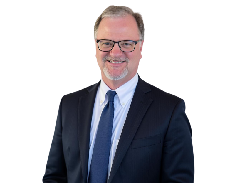 Ken Sulzer in a dark suit, white shirt, and blue tie, smiling in front of a light geometric background.