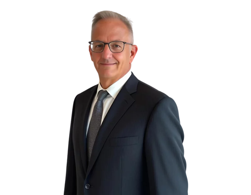 A man with short gray hair and glasses smiling subtly in a professional headshot. He is wearing a dark pinstripe suit, white shirt, and a textured dark tie, standing against a plain background.