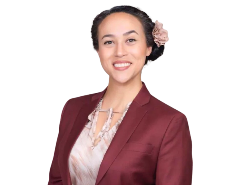 Arcelia Magaña wearing a burgundy blazer over a patterned blouse, with their dark hair styled back and adorned with a light pink flower, posed in front of a blue and white geometric background.