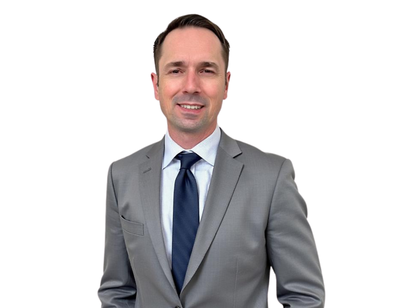 John Babione in a light gray suit with a white shirt and dark navy tie smiles against a light blue and white geometric background.
