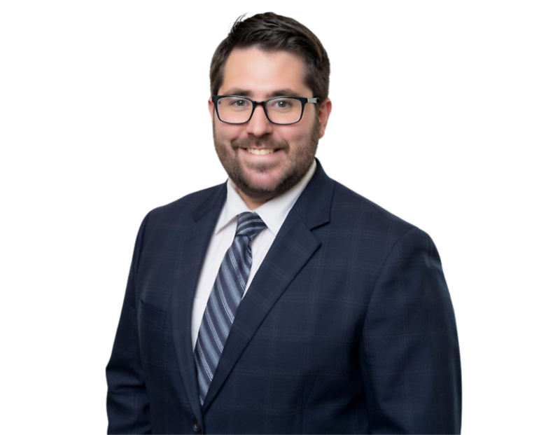 Smiling man with dark hair, beard, and glasses wearing a dark plaid suit, white shirt, and striped tie. He is standing against a transparent background.