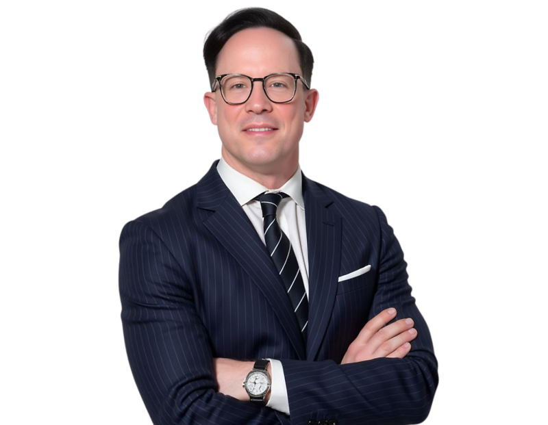 Smiling professional man with short dark hair and round glasses wearing a navy pinstripe suit, white dress shirt, and striped tie. He stands with arms crossed against a transparent background, projecting a confident and polished executive presence.
