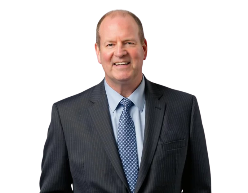 Sean Hoar in a dark pinstriped suit, light blue shirt, and patterned tie, smiling confidently against a transparent background. His posture and attire suggest a professional or corporate setting.