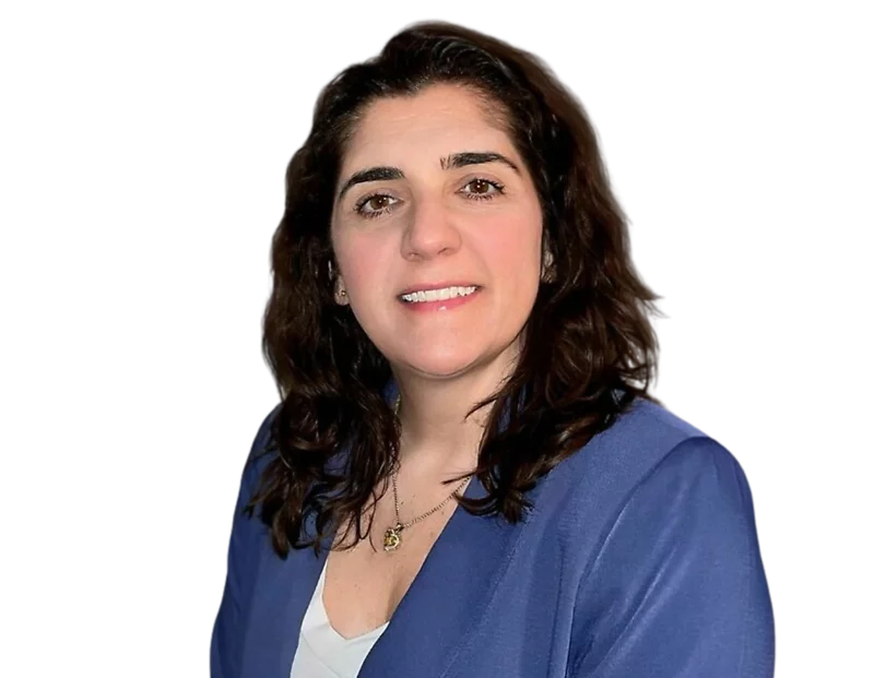 Julie Hess, smiling, wearing a blue blazer over a white top and a delicate necklace, against a plain background.