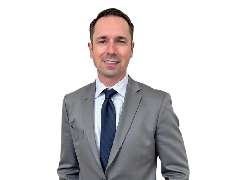John Babione in a light gray suit with a white shirt and dark navy tie smiles against a light blue and white geometric background.