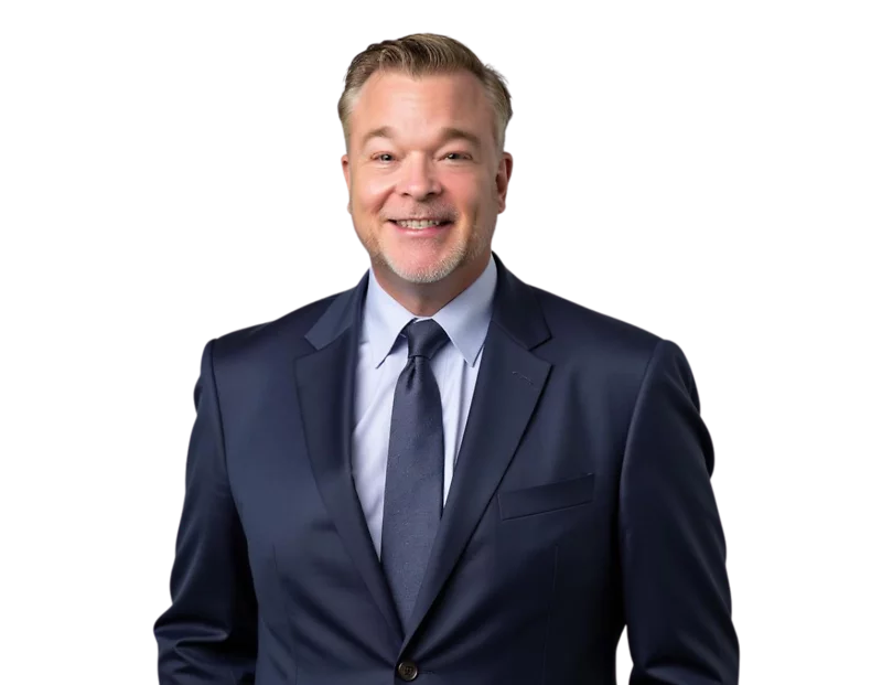 Jason Cherry in a dark navy suit and tie smiles while standing against a light blue and white geometric background.