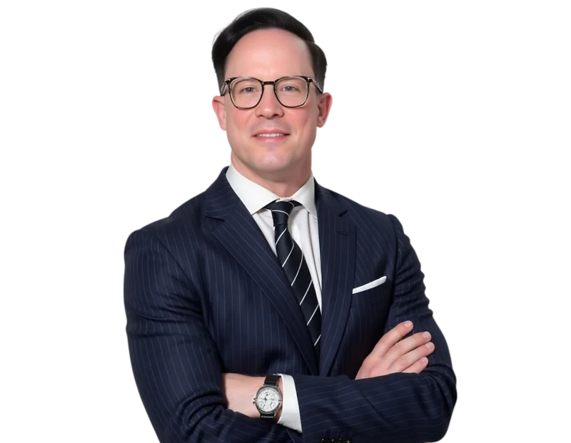 Smiling professional man with short dark hair and round glasses wearing a navy pinstripe suit, white dress shirt, and striped tie. He stands with arms crossed against a transparent background, projecting a confident and polished executive presence.