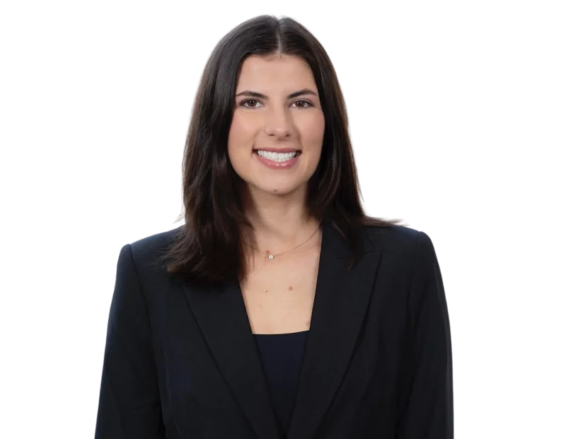 Headshot of a woman with shoulder-length dark brown hair, wearing a black blazer over a dark top. She is smiling and facing forward, with a plain background that emphasizes a professional and polished appearance.