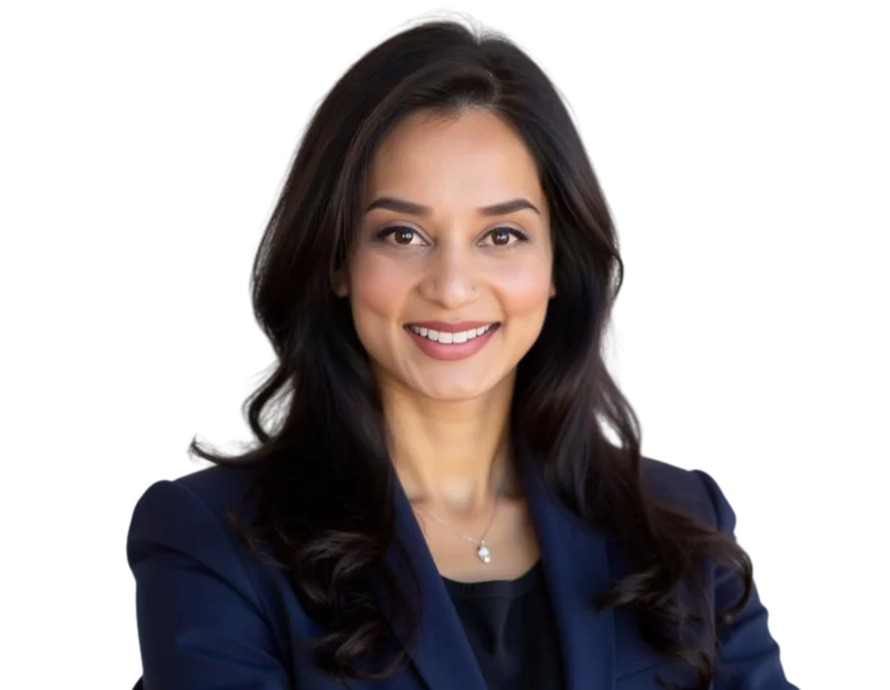 Professional woman with long, dark wavy hair wearing a navy blazer and black top, smiling confidently at the camera against a transparent background. She wears a small pendant necklace and has a polished, approachable look suitable for business or corpora