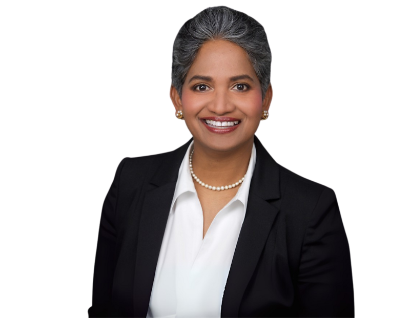 Piyumi Samaratunga in a dark suit, white blouse, and pearl necklace, smiling in front of a light geometric background.