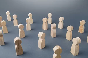 Several small wooden figurines shaped like simplified human figures are arranged on a gray surface. The scattered positioning suggests concepts of community, networking, or social distancing.