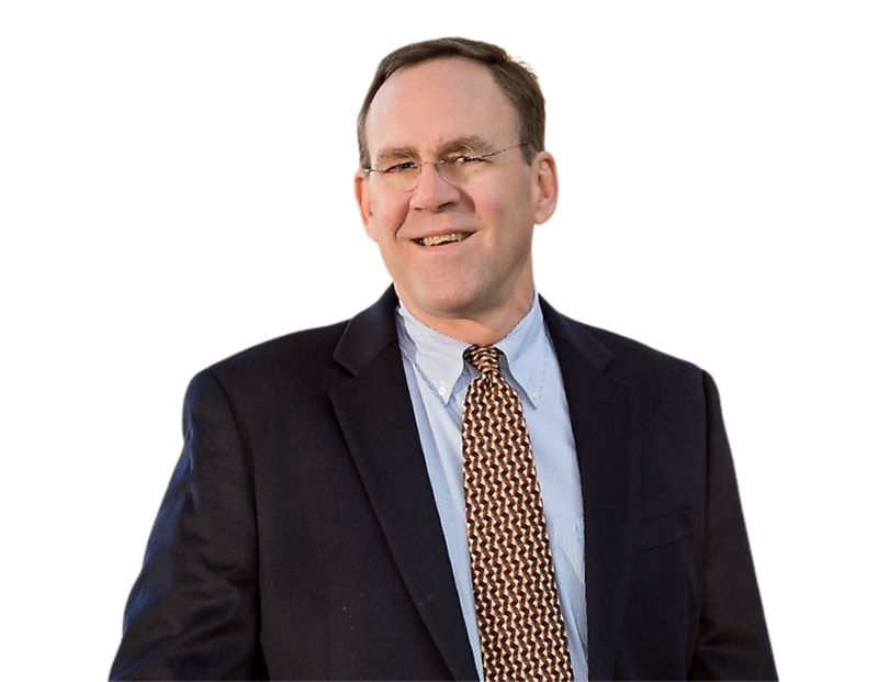 Jim Coleman in a dark blazer, light blue button-down shirt, and a geometric patterned tie, standing confidently against a transparent background. His relaxed posture and business attire convey a professional yet approachable demeanor.