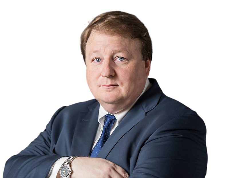Photo of Damon Kitchen wearing a navy blue suit, white shirt, and blue patterned tie, with a watch on his wrist, against a plain background.
