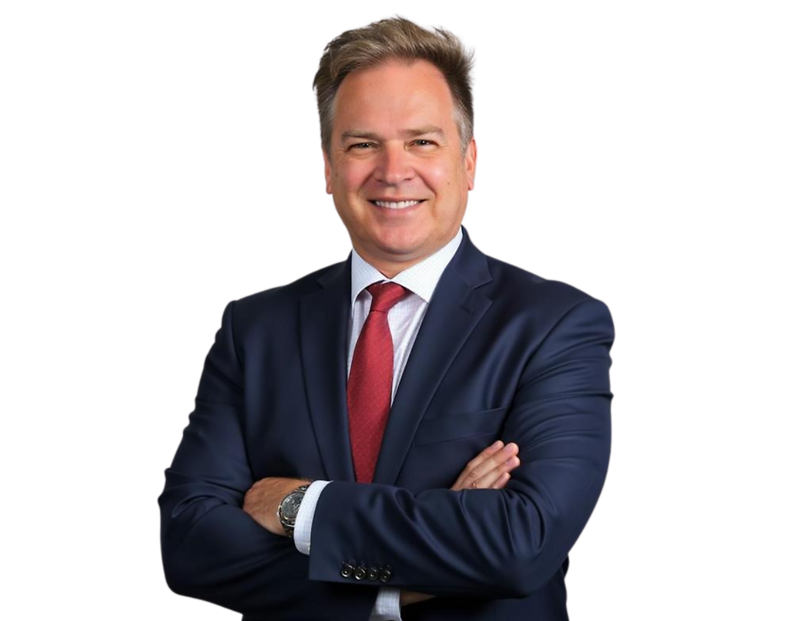 John MacDonald in a dark blue suit, white shirt, and red tie, smiling in front of a light geometric background.