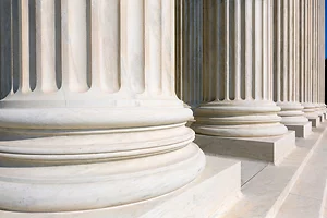 Close-up view of the marble bases of large fluted columns, showing their smooth, rounded detailing and sturdy architectural design. The perspective emphasizes strength, stability, and the grandeur of classical architecture often seen in government.