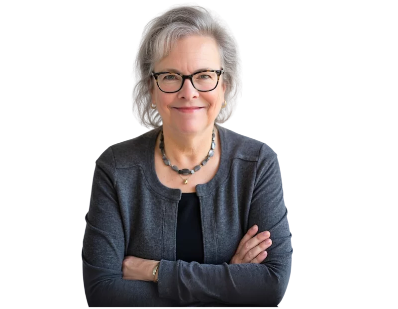 Smiling older woman with short gray hair and glasses, wearing a dark gray cardigan over a black top and a beaded necklace, with arms confidently crossed. She has a warm, approachable demeanor and a professional presence against a transparent background.