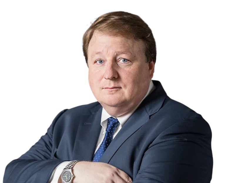 Photo of Damon Kitchen wearing a navy blue suit, white shirt, and blue patterned tie, with a watch on his wrist, against a plain background.