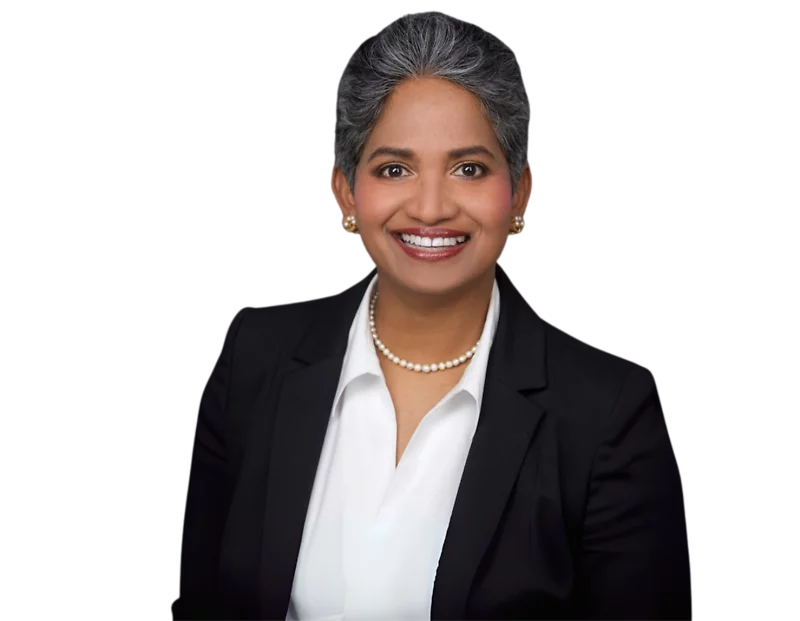 Piyumi Samaratunga in a dark suit, white blouse, and pearl necklace, smiling in front of a light geometric background.