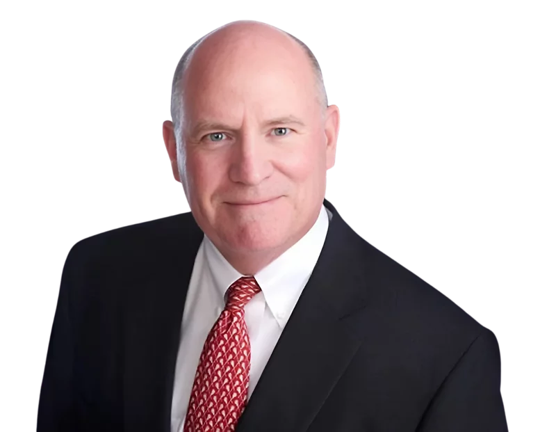 A middle-aged man with a bald head smiles slightly while wearing a black suit, white dress shirt, and red patterned tie. The background has been removed, highlighting him in a clean, professional headshot.