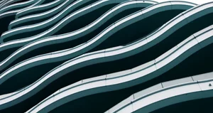 A modern building facade features undulating white balcony edges that create a flowing wave pattern across multiple floors. The dark recesses between balconies emphasize the rhythmic curves and minimalist design.