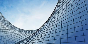 Curved glass facade of a modern skyscraper reflecting the blue sky, creating a flowing, wave-like architectural form. The sleek grid of windows emphasizes both elegance and futuristic design.