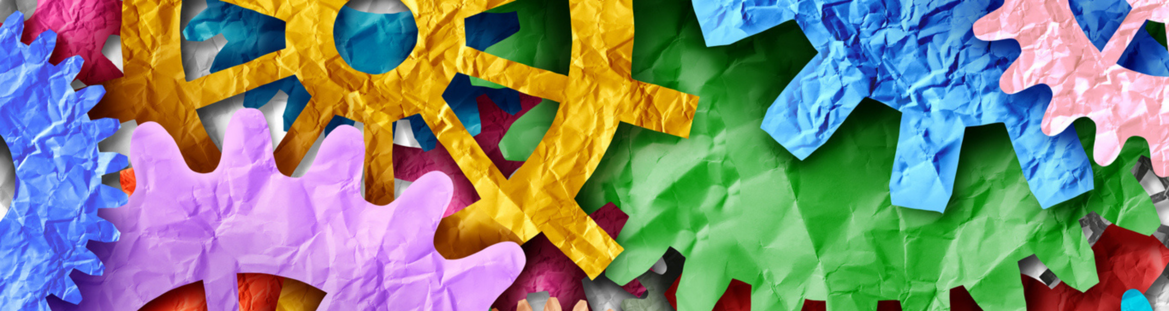 Colorful crinkled-paper gears in purple, yellow, green, blue and red interlock, symbolizing coordinated workplace systems and teamwork.
